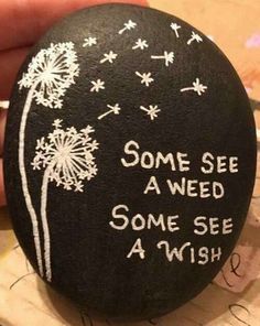 someone is holding a rock with some writing on it and dandelions in the background