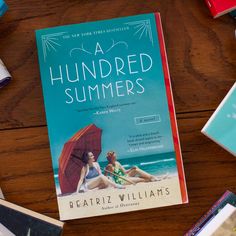 a book titled a hundred summers sitting on top of a wooden table next to books