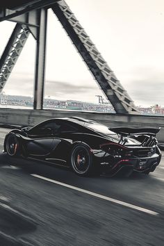 a black sports car driving on the road next to a tall metal structure with a bridge in the background