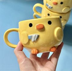 two yellow mugs with faces on them are being held by someone's hand