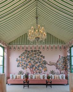 a pink couch sitting under a chandelier in a room with green and white striped walls