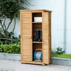 a tall wooden storage cabinet sitting next to a wall with plants and trees in the background