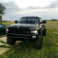 a large black truck parked on top of a grass covered field next to a car