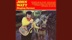 a man holding a guitar and standing next to a horse with a yellow shirt on