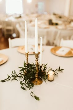 the centerpieces on this table are adorned with greenery and gold candlesticks