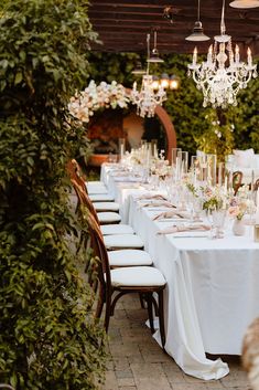 a long table with white linens and chandeliers is set up for a formal dinner