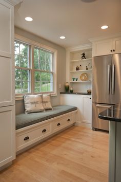 a kitchen with white cabinets and wood flooring next to a stainless steel refrigerator freezer