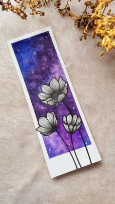 a card with flowers on it sitting next to some dried plants and purple space in the background