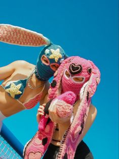 a woman in bunny ears holding a pink stuffed animal next to a tennis court net