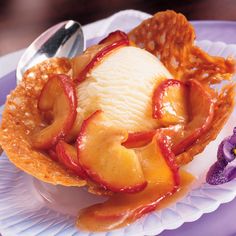 an ice cream sundae on a paper plate with a spoon and purple flowers in the background