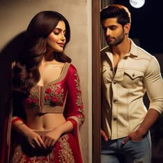 a man standing next to a woman in a red lehenga and white shirt