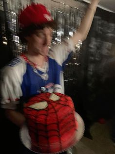 a person holding a cake in their hand and wearing a spiderman costume on it