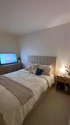 a bed with white sheets and pillows in a bedroom next to a tv mounted on the wall