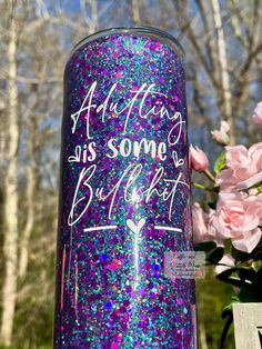 there is a purple and blue glittered cup with writing on it next to pink flowers