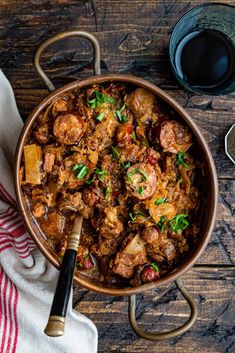 a bowl filled with meat and vegetables on top of a wooden table next to a glass of wine