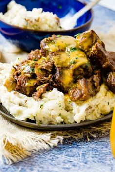 a plate with mashed potatoes and beef covered in gravy next to a blue bowl