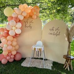 an arch made out of balloons with writing on it and some chairs in the grass