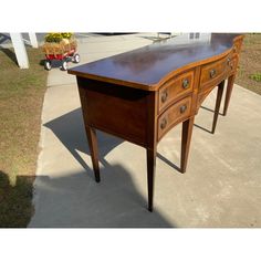 a wooden desk sitting on top of a cement floor next to a sidewalk and grass