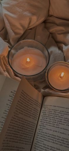 an open book sitting on top of a bed next to two lit candles in a glass bowl