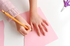 a child's hand on top of a piece of pink paper with a pencil