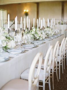 a long table is set with white flowers and candles for an elegant dinner party or reception