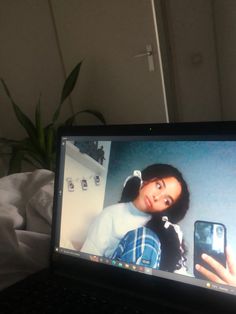 an open laptop computer sitting on top of a bed next to a potted plant