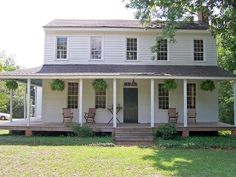 a white two story house with porches and chairs on the front lawn, surrounded by trees