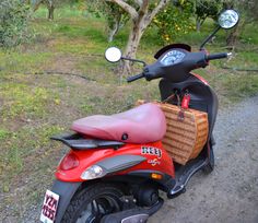 a red scooter with a basket on the back parked in front of some trees