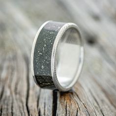 a wedding ring with black and white speckles on it sitting on a wooden surface