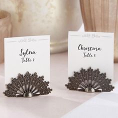 two place cards are placed next to each other on a table with a vase in the background