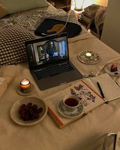 an open laptop computer sitting on top of a bed next to plates and cups filled with food