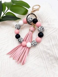 a pink tasseled keychain with black and white beads on it next to a plant