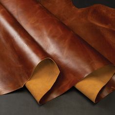 two pieces of brown leather on a black surface with one piece cut out and the other half rolled up