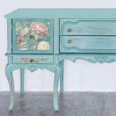 a blue dresser with flowers painted on the front and side drawers, sitting against a white wall