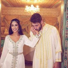 a man standing next to a woman in front of a mirror wearing a white dress