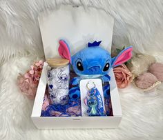 a blue stuffed animal in a white box on a furry surface next to some flowers