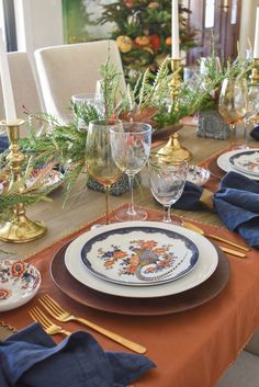 the table is set with plates, silverware and gold candlesticks for christmas dinner