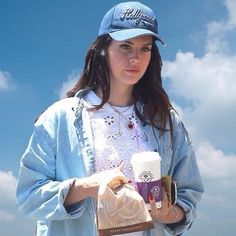 a young woman holding a coffee cup and paper bag in her hand while standing on the beach