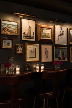 several framed pictures hang on the wall above two bar stools with candles in front of them