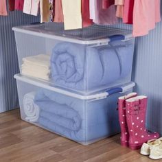 two plastic storage containers are stacked on top of each other in front of clothes and rain boots