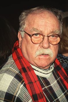 an older man with glasses and a red scarf is looking off to the side while standing in