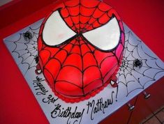 a spiderman birthday cake on top of a red table with white and black frosting