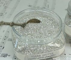 two jars filled with silver glitter sitting on top of sheet music paper and musical notes