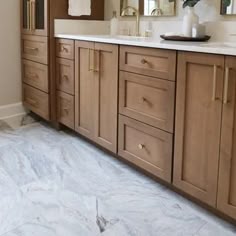 a bathroom with marble flooring and wooden cabinetry is pictured in this image, there are two mirrors on the wall above the vanity