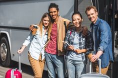 four people are standing in front of a bus with their luggage and smiling at the camera