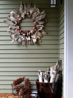 a wreath is hanging on the side of a house with pine cones and other decorations