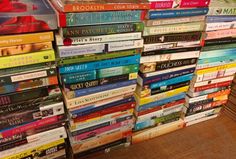 a large stack of books sitting on top of a wooden floor next to a wall