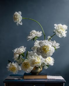 a vase filled with white and yellow flowers on top of a blue table next to a book