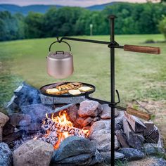 an outdoor grill with food cooking over it in the middle of some rocks and grass