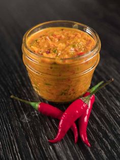 a glass jar filled with curry next to a red chili pepper on a wooden table